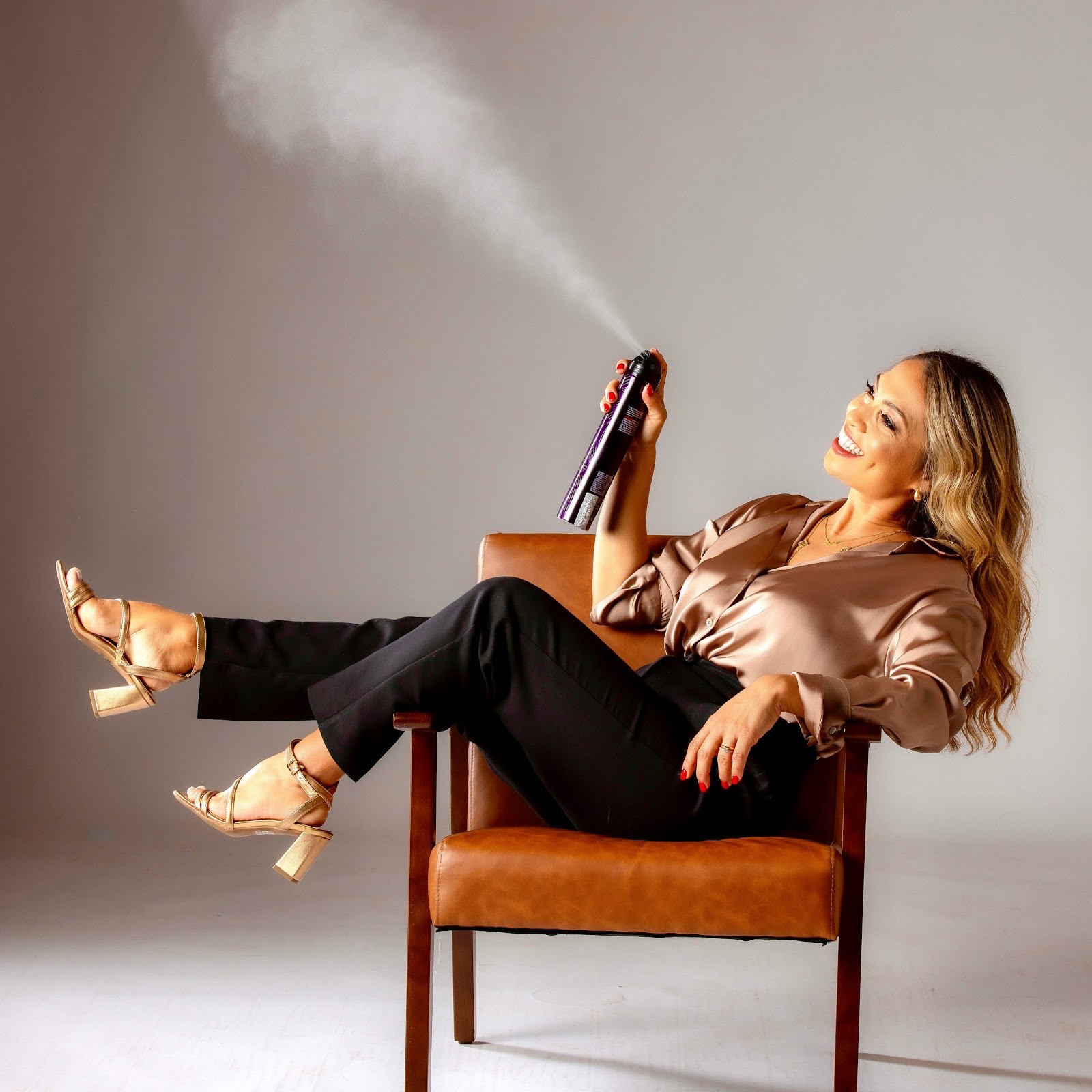 A Musart Salon stylist in a champagne satin blouse relaxes in a chair, finishing a style with a cloud of hairspray