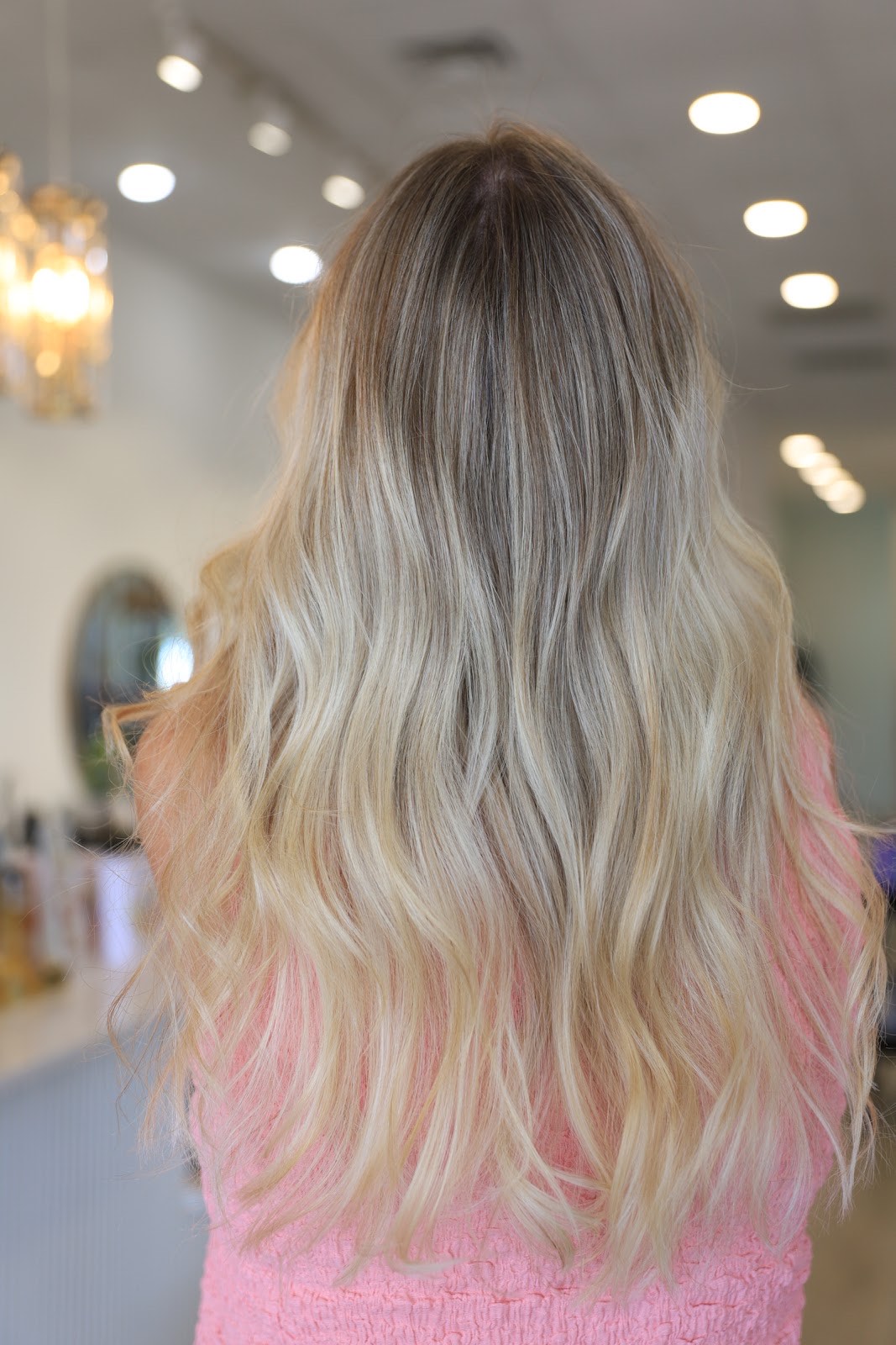 Long blonde balayage waves with rooted dimension under salon lighting